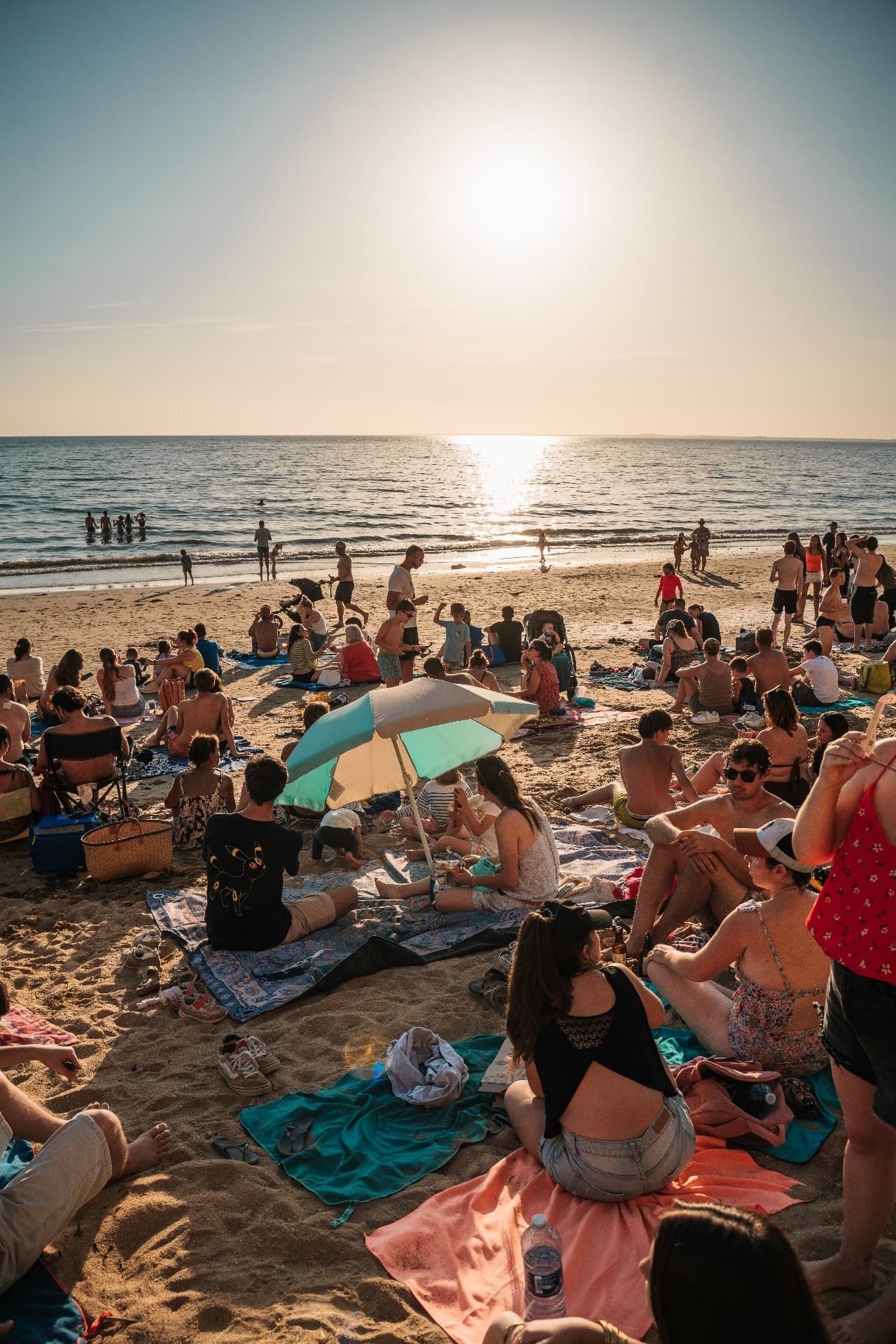 Busy beach at sunset with people relaxing on the sand
