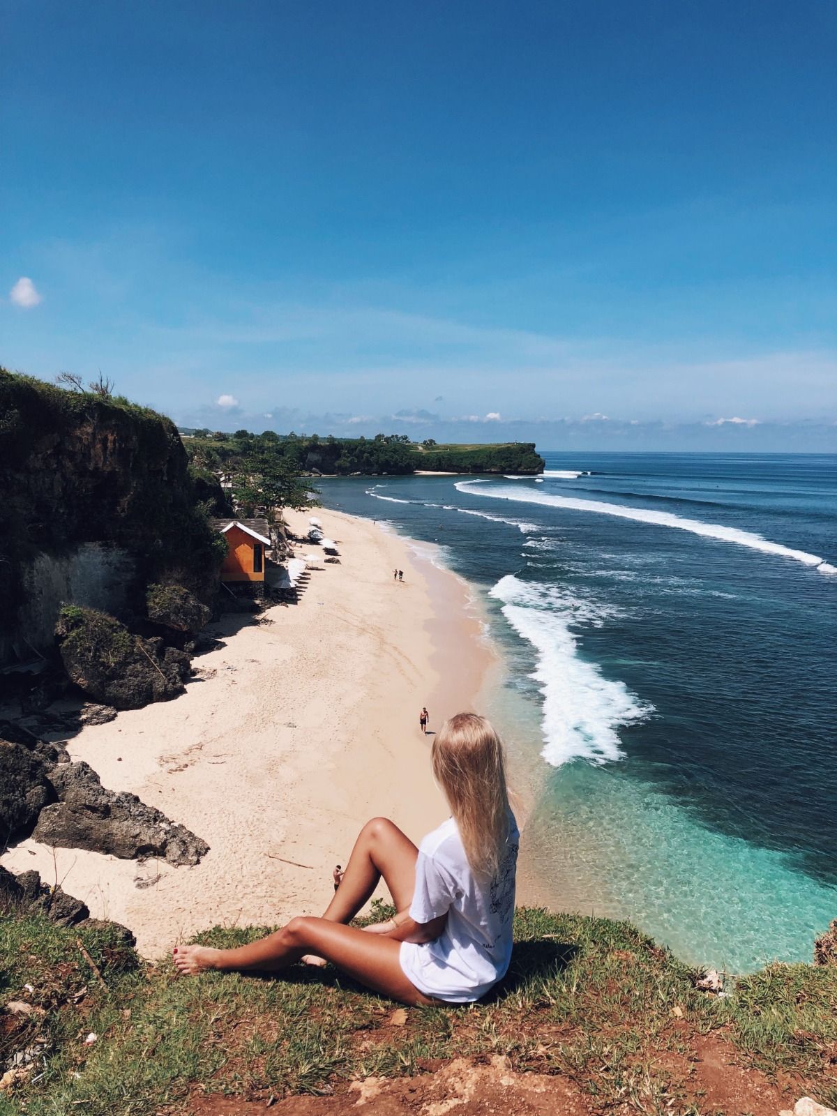 Woman sitting on a grassy clifftop above a turquoise beach