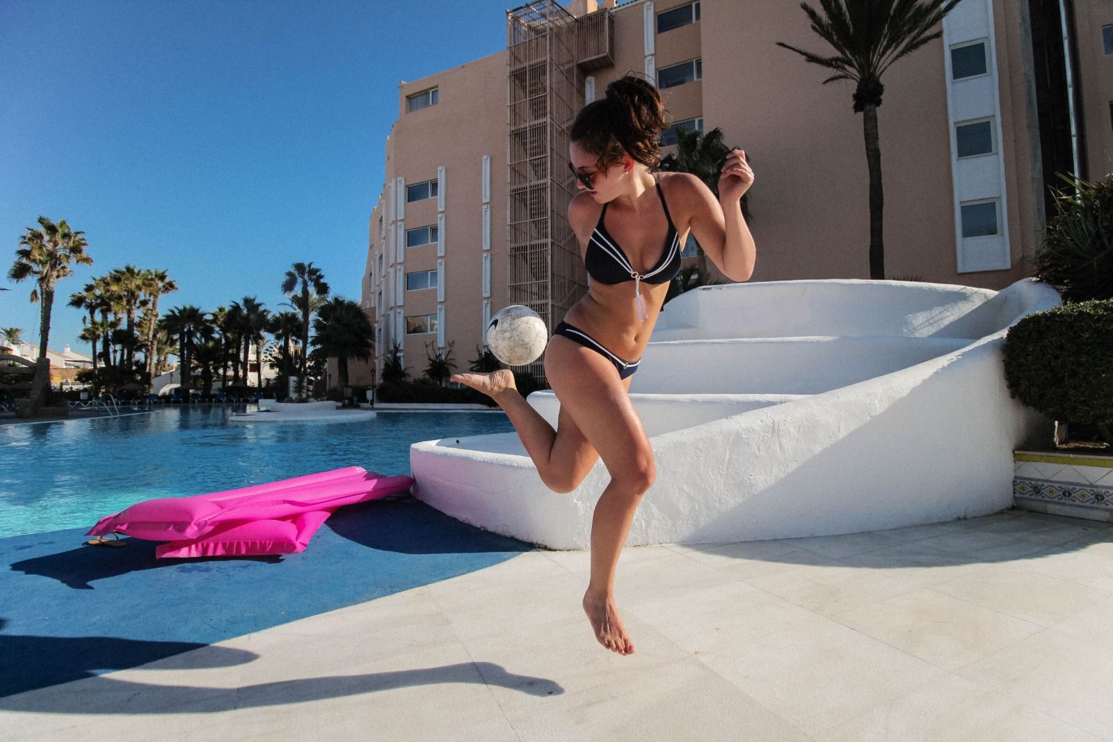 Girl keeping a football up on a sunny poolside terrace at a hotel