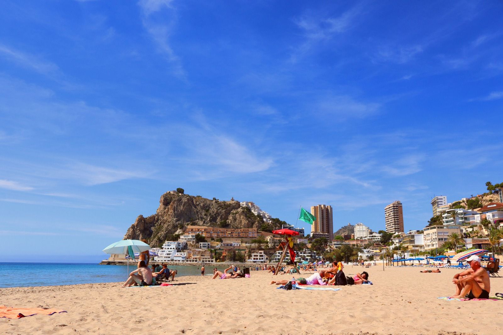 Busy Spanish sandy beach with sunbathers and a rocky headland behind