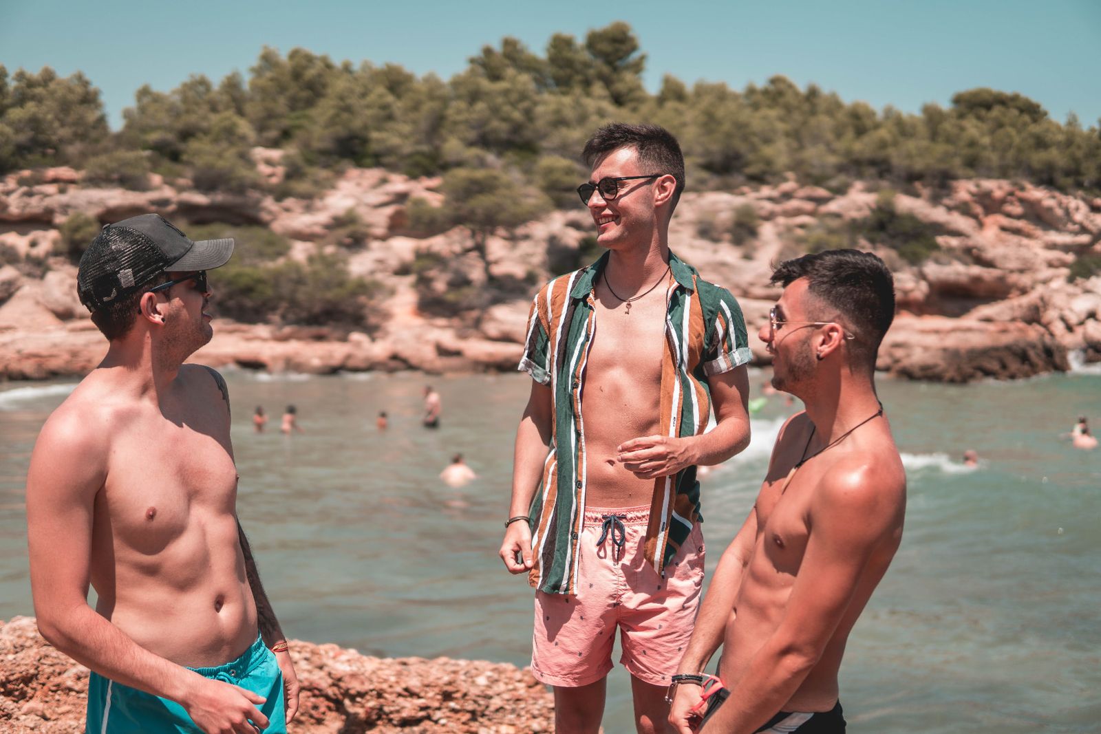 Three friends talking and laughing on rocks by the sea
