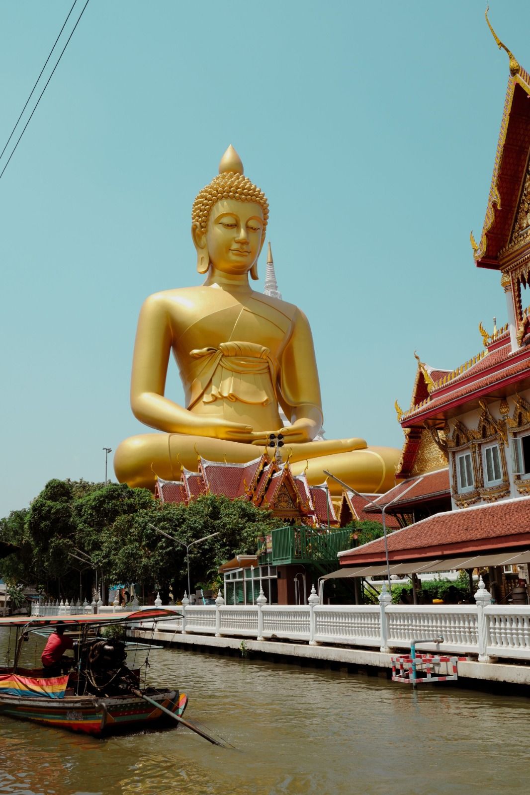 Gold Buddha statue beside a Bangkok canal with a longtail boat