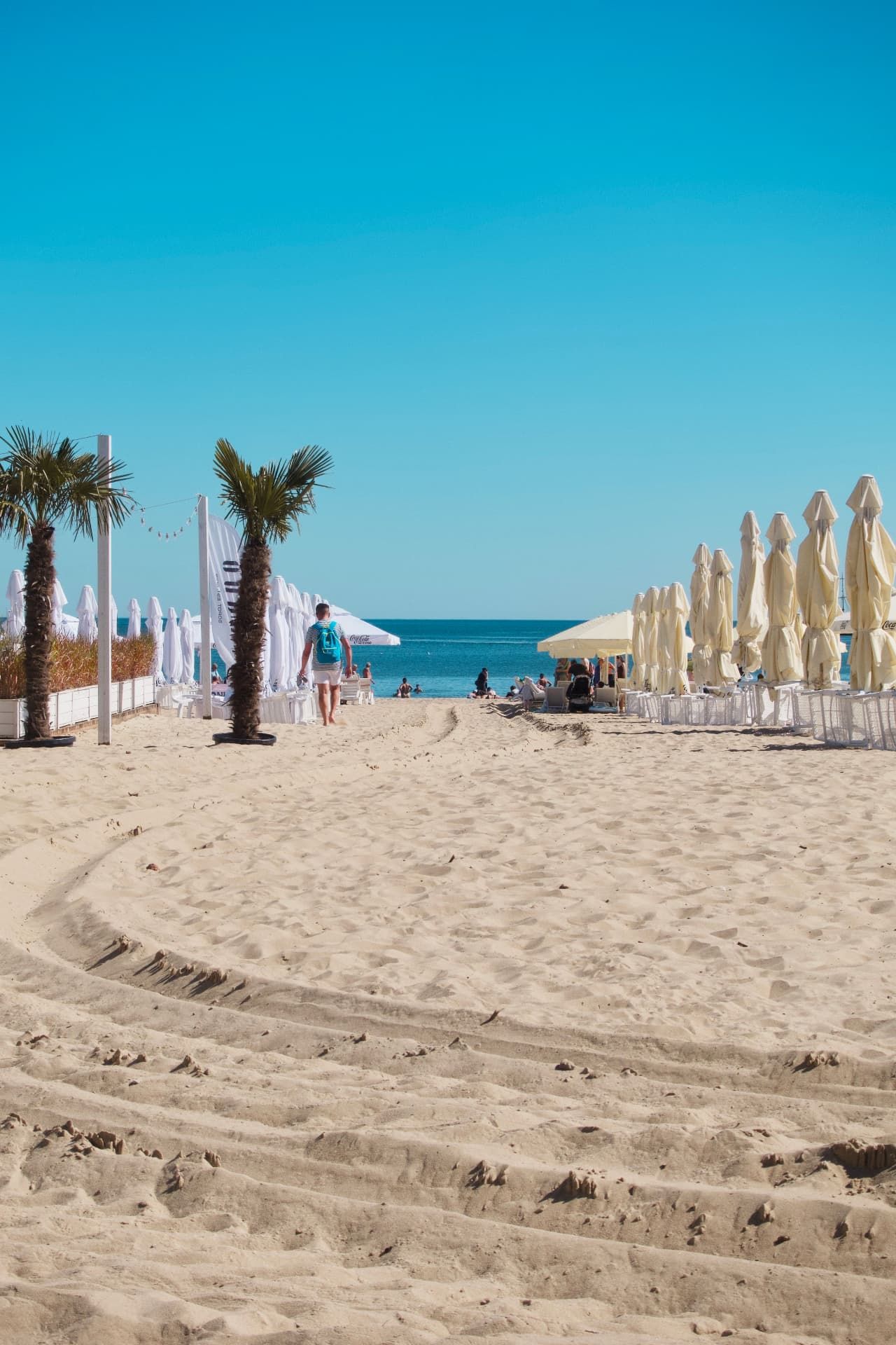 Sandy path between white beach umbrellas leading to the sea